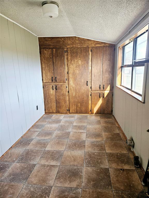 unfurnished bedroom featuring a textured ceiling, lofted ceiling, and wooden walls