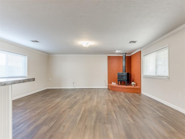 unfurnished living room with hardwood / wood-style floors, a wood stove, ornamental molding, and a healthy amount of sunlight