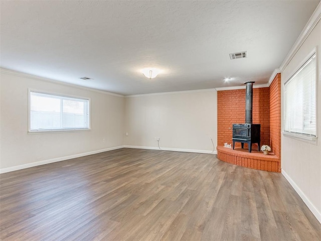 unfurnished living room featuring hardwood / wood-style flooring, a healthy amount of sunlight, a wood stove, and crown molding