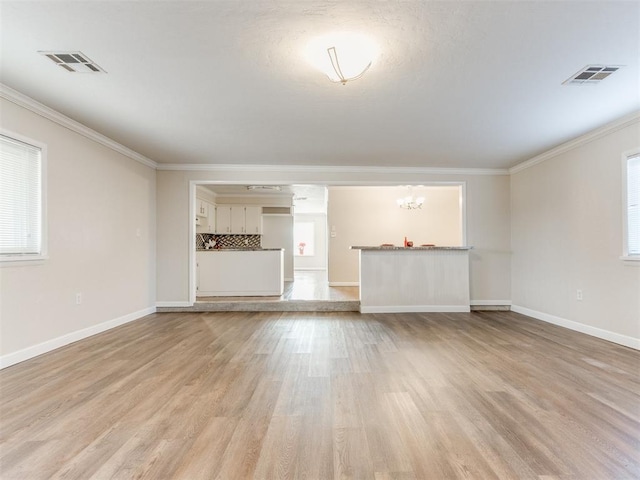 unfurnished living room with crown molding, light hardwood / wood-style floors, and an inviting chandelier