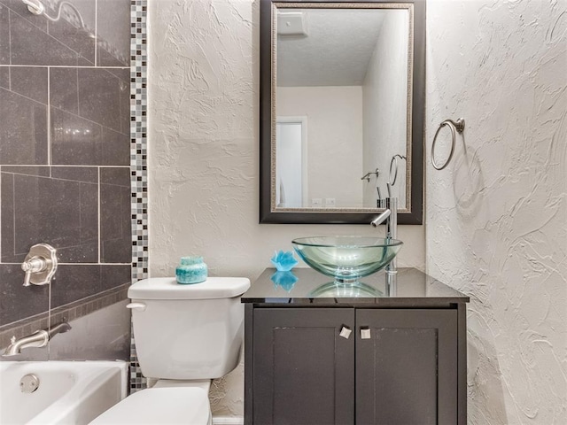 bathroom with a textured ceiling, vanity, toilet, and a tub