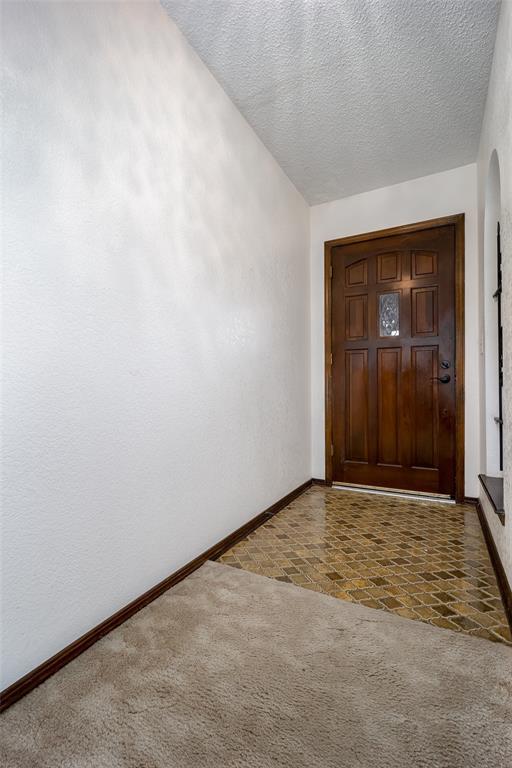 foyer entrance featuring dark carpet and a textured ceiling