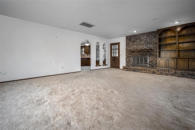 unfurnished living room featuring carpet flooring, a textured ceiling, and a brick fireplace