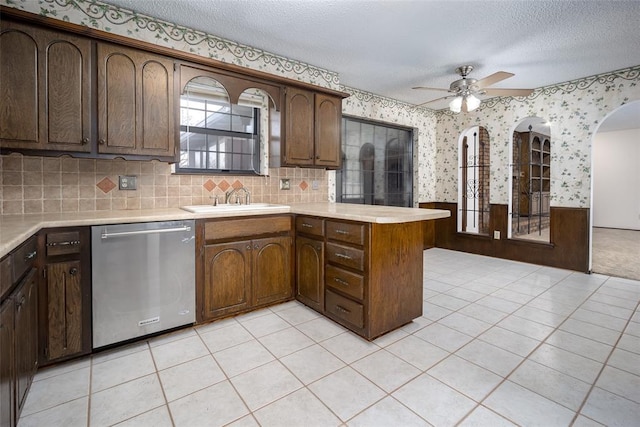 kitchen with ceiling fan, sink, stainless steel dishwasher, kitchen peninsula, and a textured ceiling