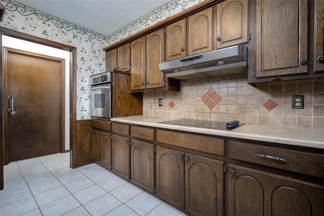 kitchen featuring stainless steel oven, black electric cooktop, a textured ceiling, and light tile patterned floors