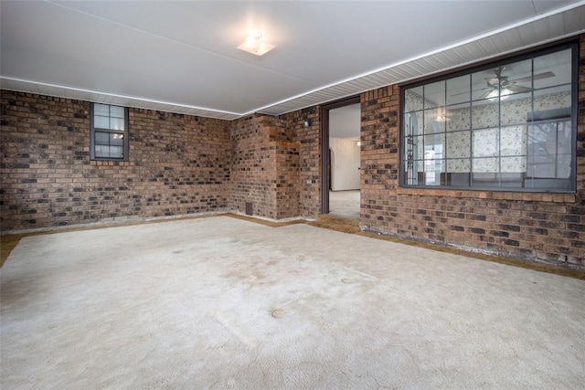 unfurnished living room with ceiling fan, carpet, and brick wall