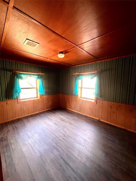 empty room with a healthy amount of sunlight, dark hardwood / wood-style floors, and wooden ceiling