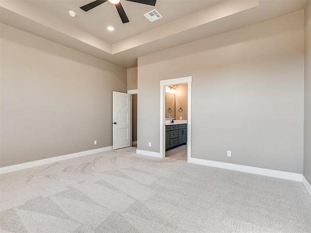 carpeted bedroom with ceiling fan, a raised ceiling, and ensuite bath