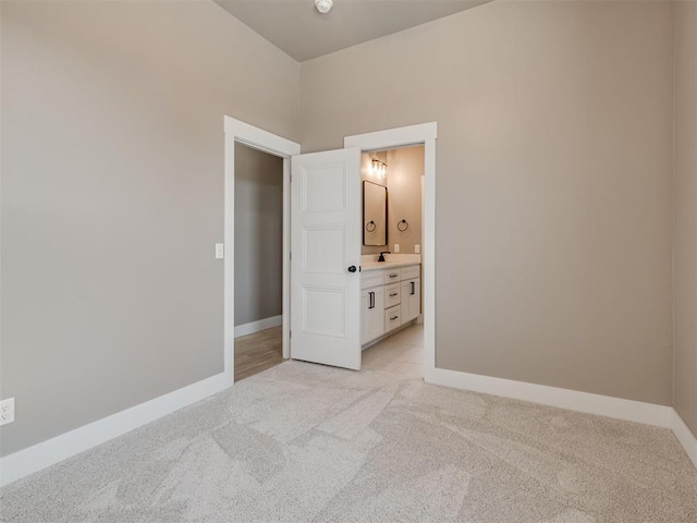 unfurnished bedroom featuring ensuite bath, light carpet, and sink