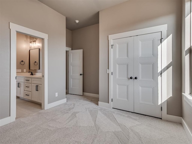 unfurnished bedroom with light colored carpet, ensuite bath, a closet, and sink