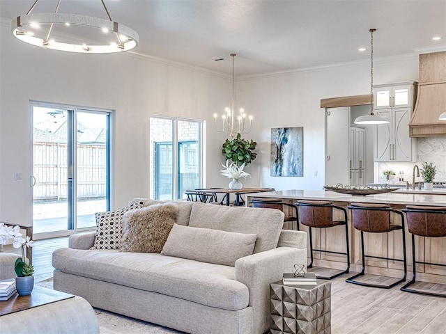 living room with crown molding, light wood-type flooring, sink, and a chandelier