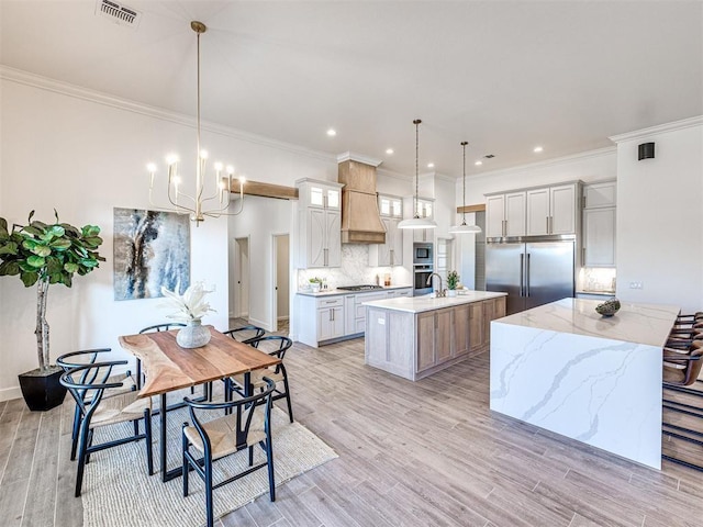 kitchen with a large island with sink, built in appliances, light hardwood / wood-style flooring, and pendant lighting