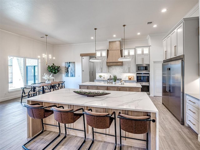 kitchen with backsplash, decorative light fixtures, light wood-type flooring, a large island, and stainless steel appliances