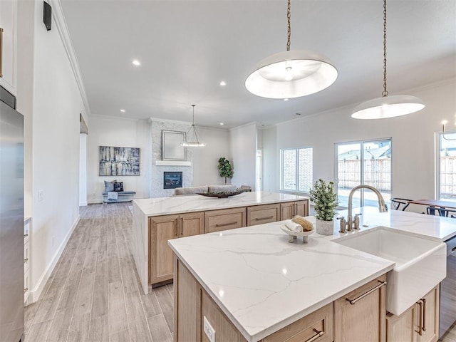 kitchen featuring light brown cabinetry, a large fireplace, sink, a large island with sink, and pendant lighting