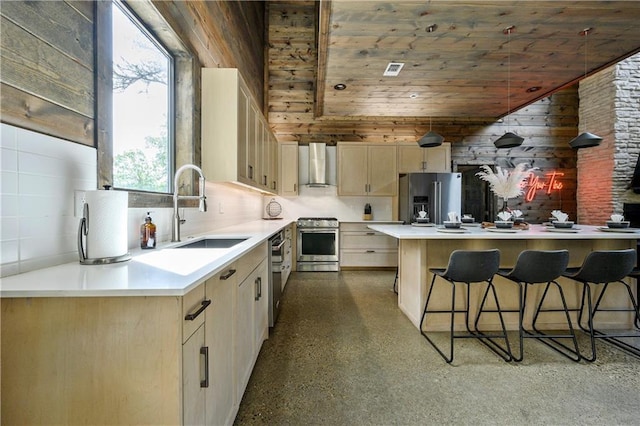 kitchen with lofted ceiling, wall chimney range hood, sink, wooden walls, and stainless steel appliances