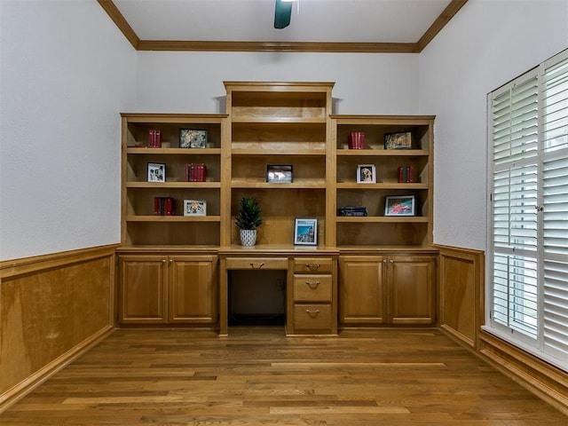 unfurnished office featuring hardwood / wood-style floors, crown molding, built in desk, and wooden walls