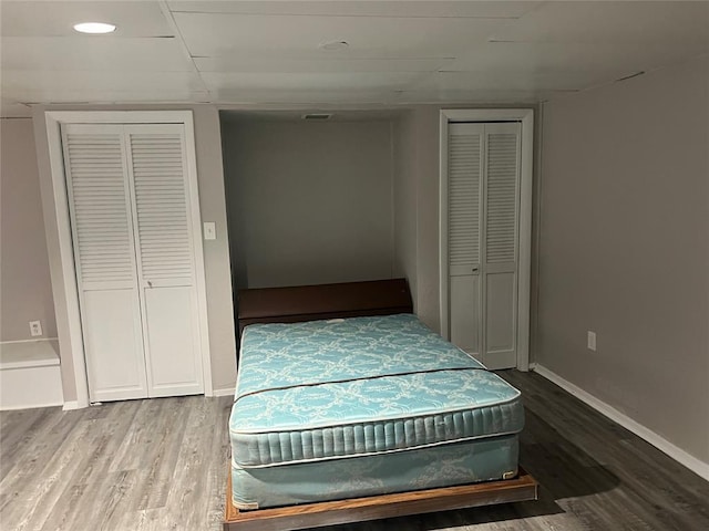 bedroom with wood-type flooring and two closets