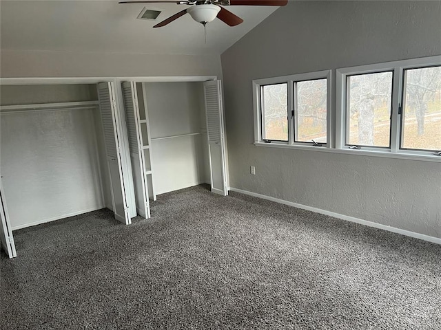 unfurnished bedroom with lofted ceiling, dark carpet, ceiling fan, and multiple closets