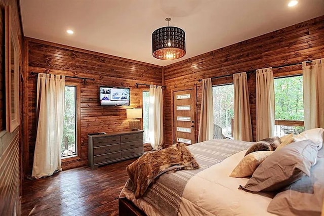 bedroom with access to outside, wood walls, and dark wood-type flooring