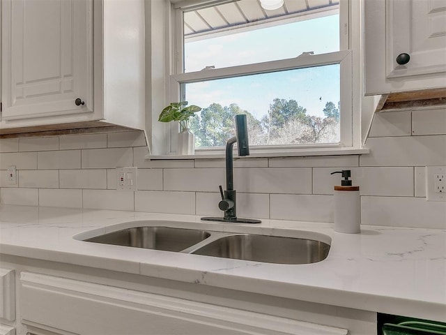 interior details featuring white cabinetry, decorative backsplash, sink, and light stone counters