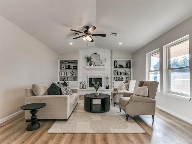 living room featuring built in shelves, ceiling fan, a brick fireplace, light hardwood / wood-style floors, and lofted ceiling