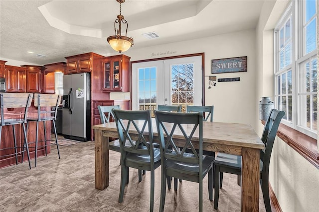 dining space with a raised ceiling, french doors, and a textured ceiling