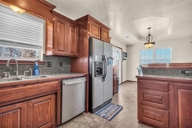 kitchen with sink, stainless steel appliances, pendant lighting, a textured ceiling, and a tray ceiling