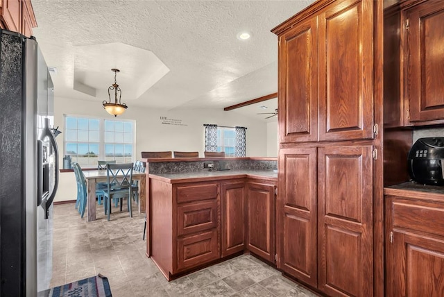 kitchen with ceiling fan, stainless steel refrigerator with ice dispenser, kitchen peninsula, a textured ceiling, and decorative light fixtures