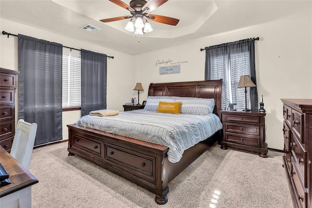 bedroom featuring light carpet, a tray ceiling, and ceiling fan