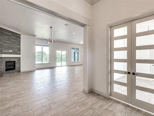 foyer with a notable chandelier, a tiled fireplace, crown molding, and french doors