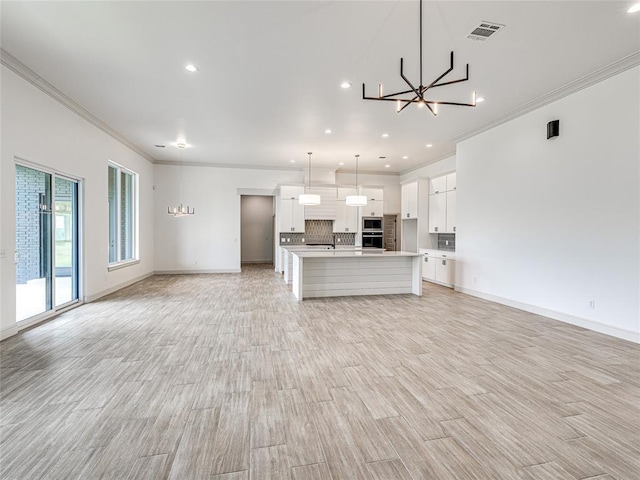 kitchen featuring stainless steel microwave, a center island with sink, white cabinets, decorative backsplash, and decorative light fixtures