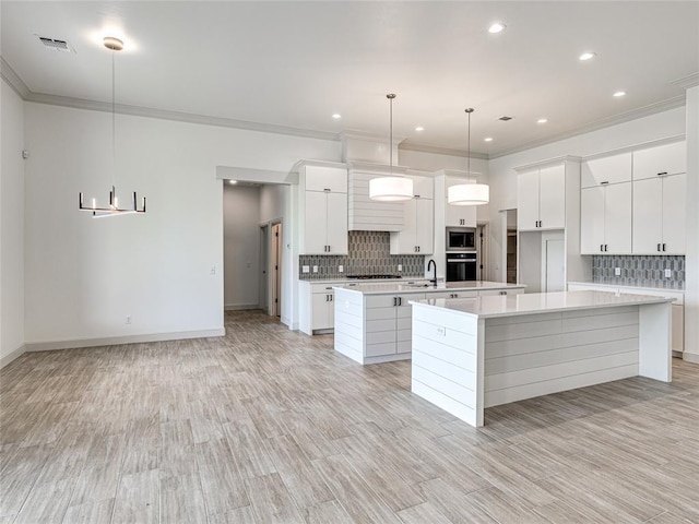 kitchen featuring a large island with sink, white cabinets, oven, built in microwave, and decorative light fixtures