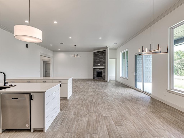 kitchen with dishwasher, hanging light fixtures, ornamental molding, a fireplace, and white cabinetry