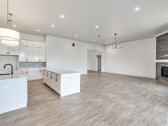 kitchen with tasteful backsplash, a kitchen island with sink, white cabinetry, hanging light fixtures, and a tiled fireplace