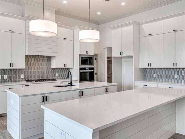 kitchen with pendant lighting, a kitchen island with sink, sink, white cabinetry, and stainless steel appliances