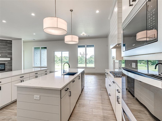 kitchen with a center island with sink, sink, hanging light fixtures, white cabinetry, and stainless steel appliances