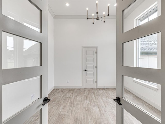 entrance foyer with a towering ceiling, ornamental molding, light wood-type flooring, and a notable chandelier