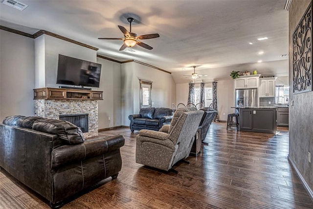 living room with ceiling fan, a stone fireplace, dark hardwood / wood-style floors, vaulted ceiling, and ornamental molding