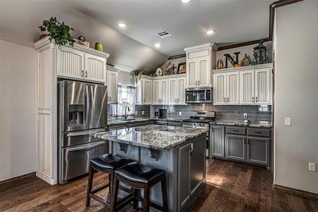 kitchen featuring appliances with stainless steel finishes, dark hardwood / wood-style flooring, a center island, and lofted ceiling