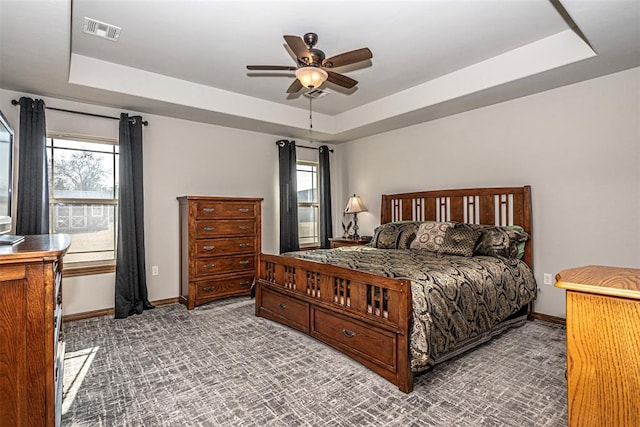 carpeted bedroom with a raised ceiling, multiple windows, and ceiling fan