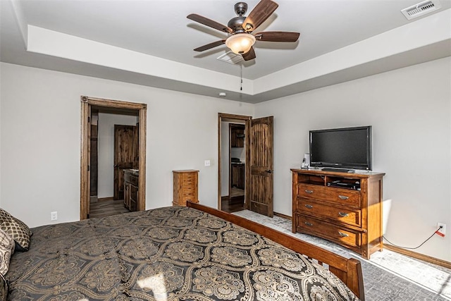 bedroom featuring ceiling fan, a raised ceiling, and ensuite bath