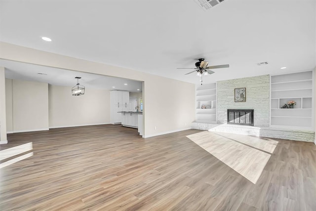 unfurnished living room featuring hardwood / wood-style flooring, ceiling fan with notable chandelier, a fireplace, and built in shelves