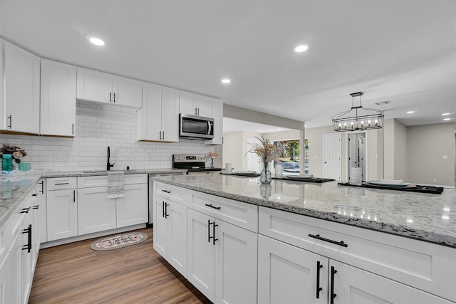 kitchen with white cabinets, light wood-type flooring, stainless steel appliances, and tasteful backsplash