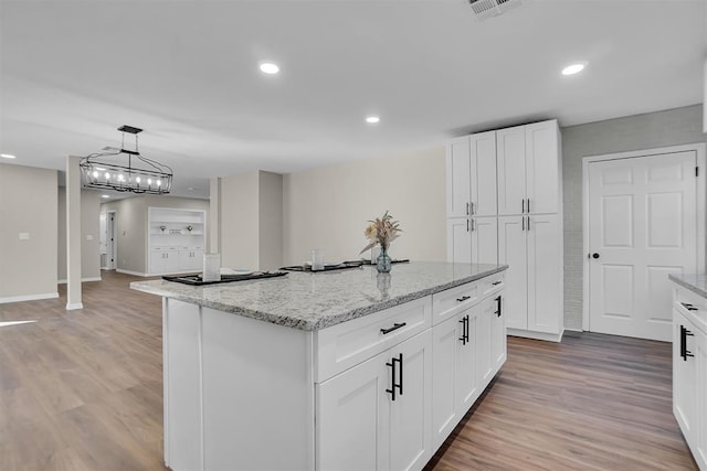 kitchen with white cabinets, light hardwood / wood-style flooring, a kitchen island, and light stone counters