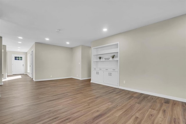 unfurnished living room with built in features and hardwood / wood-style flooring