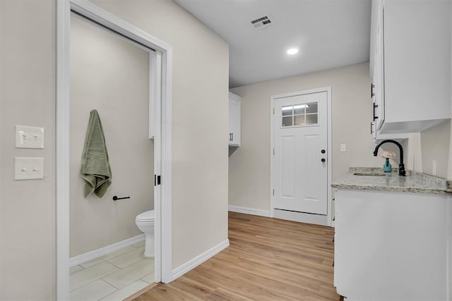 kitchen with light stone countertops, light wood-type flooring, white cabinetry, and sink