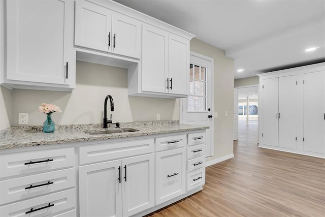 kitchen with light stone counters, white cabinetry, sink, and light hardwood / wood-style flooring