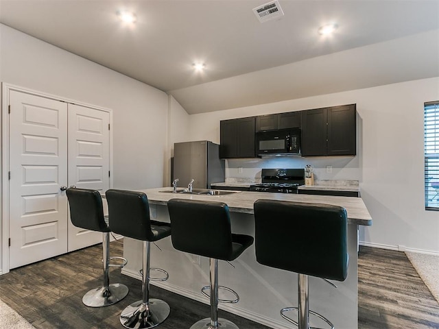 kitchen with black appliances, a center island with sink, sink, dark hardwood / wood-style flooring, and a breakfast bar area