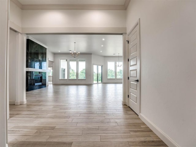 unfurnished living room featuring a notable chandelier, light hardwood / wood-style floors, crown molding, and a fireplace