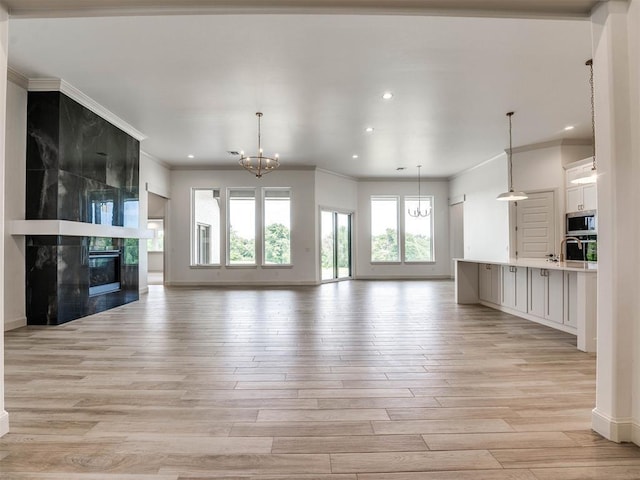 unfurnished living room with a high end fireplace, ornamental molding, a notable chandelier, and light wood-type flooring